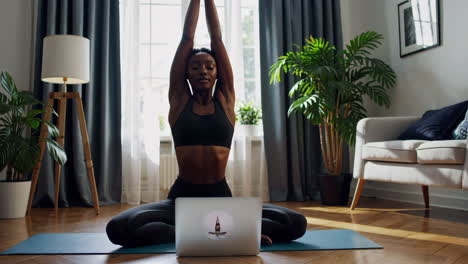 woman practicing yoga at home with an online class on her laptop