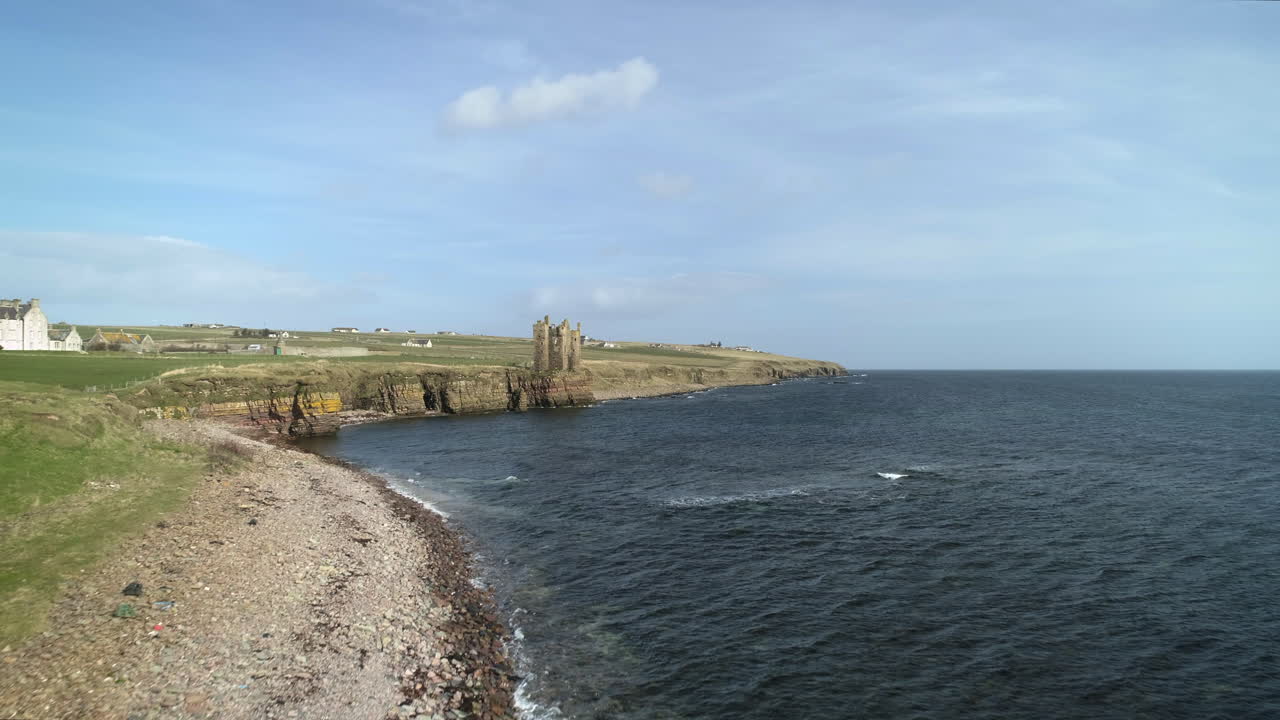disparo aéreo que se mueve a través de la costa hacia el castillo de keiss en un día soleado, caithness, escocia