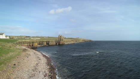 aerial rising shot moving across the coastline towards keiss castle on a sunny day, caithness, scotland