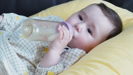 close up of an adorable baby girl drinking her milk while resting on a yellow pillow - static shot