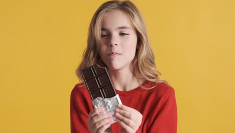 teenage caucasian girl eating chocolate bar in front of the camera.