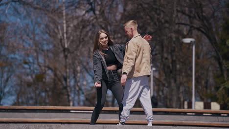 funny young couple dancing and jumping outdoors. guy and girl having joy together in the city park in sunny autumn day. happy relationships concept
