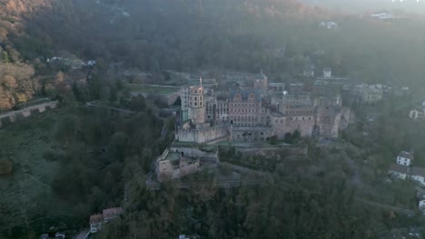 Vista-Aérea-De-Un-Castillo-Histórico,-Ubicado-En-Un-Bosque-De-árboles-Frondosos,-Mientras-Brilla-Un-Rayo-De-Sol.