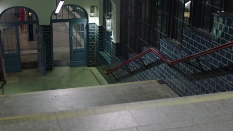 nighttime view of a tiled subway entrance with blue doors and vibrant lighting, stairs leading to a platform