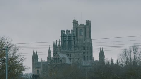 Shot-of-Ely-cathedral-with-turrets-through-trees-in-Cambridgeshire,-England-on-a-cloudy-day