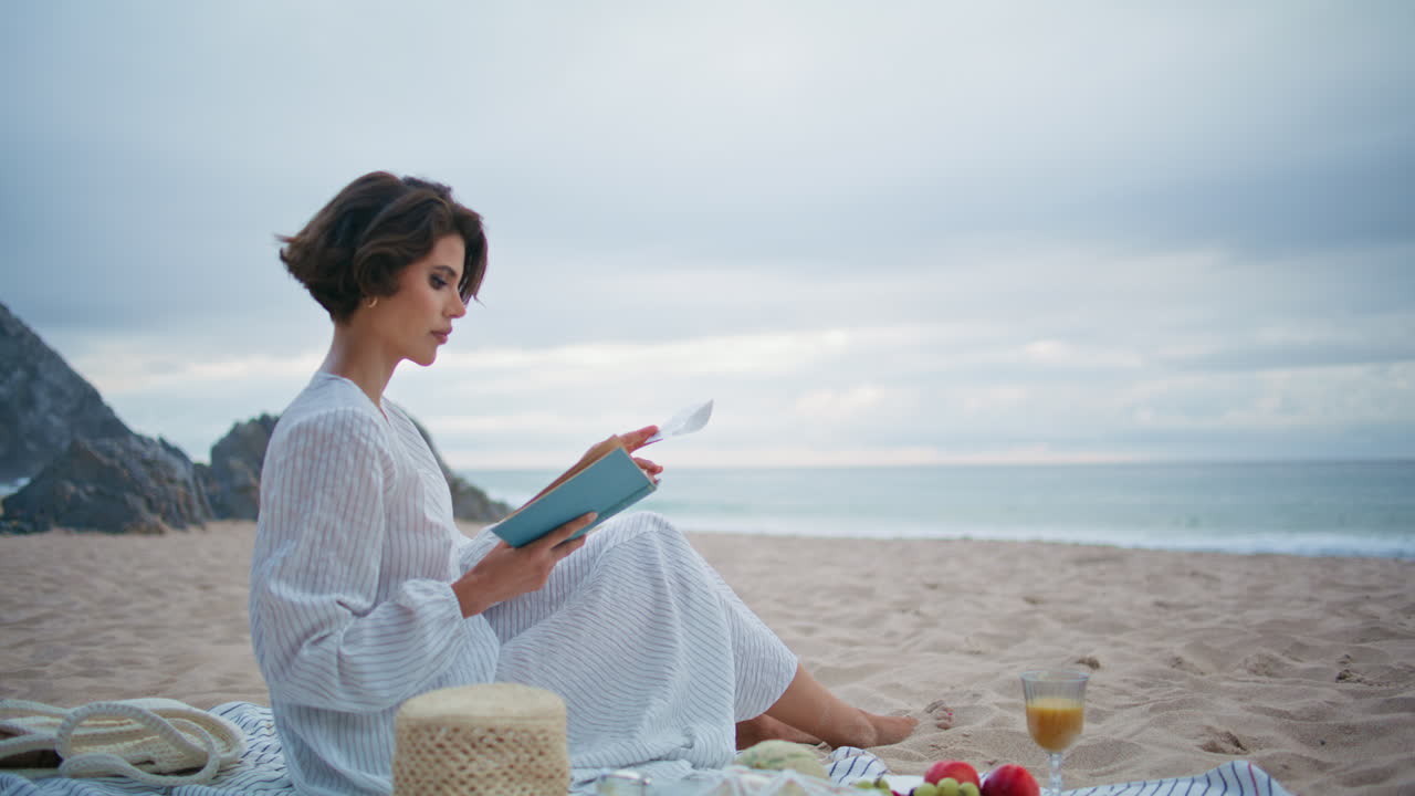 만적인 여자가 책 한 권을 들고 구름이 가득한 바가에서 아름다운 독자가 휴식을 취하고 있는 해변.