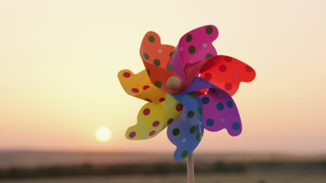 pinwheel rotate color plastic, windmill with blowing wind against the sunset sky of a sunny day summer. descending bright disk of sun beyond horizon on field with wheat sun. lens flare. relax