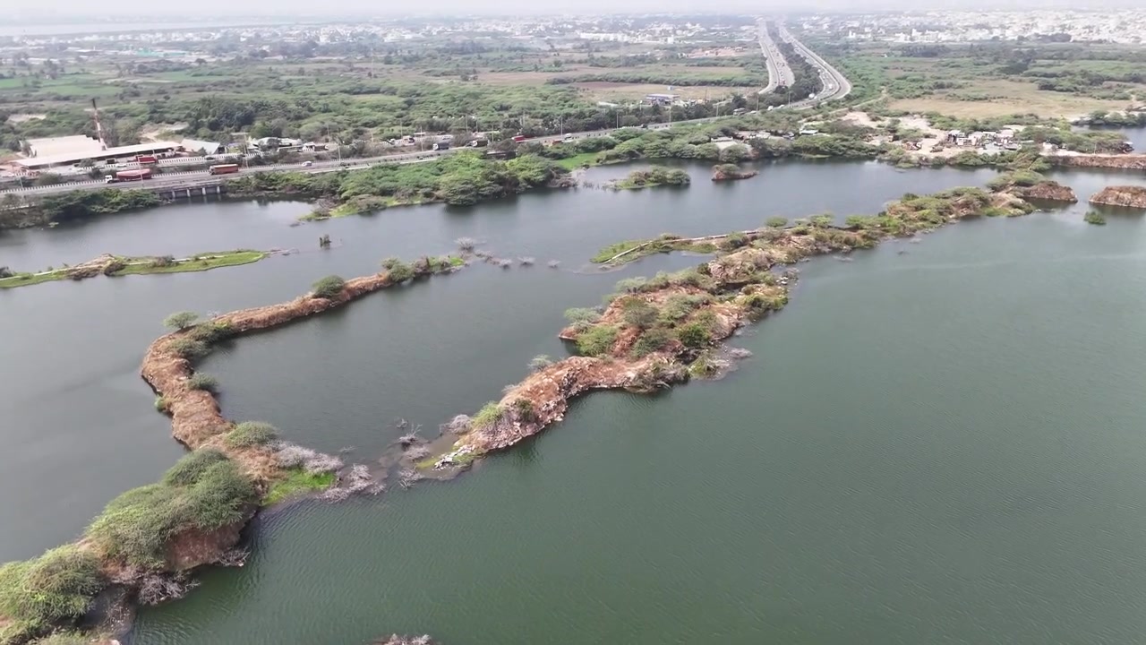 Filmisk flygvy över Sikkarayapuram granitbrott med smaragdgröna brottsjöar, oländiga granitöar och den närliggande Chennai Outer Ring Road som sträcker sig över landskapet.