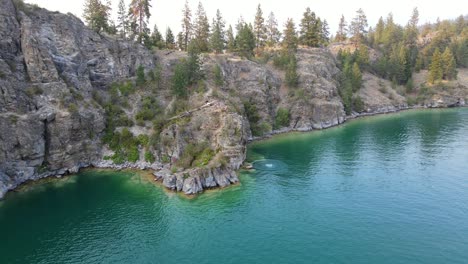 aerial view of people jumping off cliff at rattlesnake point into turquoise water of kalamalka lake