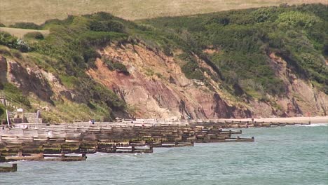 Wooden-breakwaters-in-the-sea-and-a-sandy-beach-and-hills-on-the-shoreline-in-the-English-seaside-town-of-Swanage-in-the-British-county-of-Dorset-on-the-South-coast