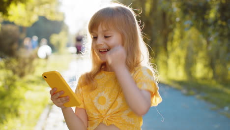 Preteen-child-girl-use-smartphone-play-online-game-celebrating-win-good-message-news-in-city-park