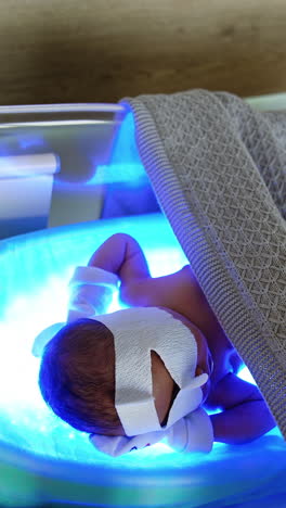newborn caucasian baby lies on uv lamp in a crib. infant having high bilirubin is cured from jaundice. vertical video