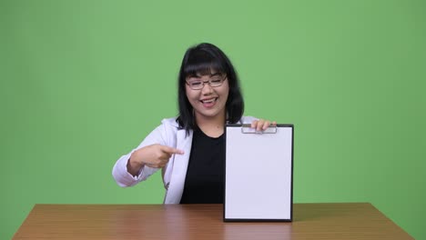 아름다운 아시아 여성 의사가 클립보드를 보여주고 엄지손가락을 올리고 있습니다.