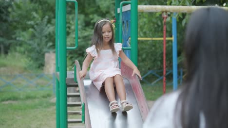 a pregnant mother and her young daughter enjoy playful time together at a playground in the park, surrounded by trees and greenery