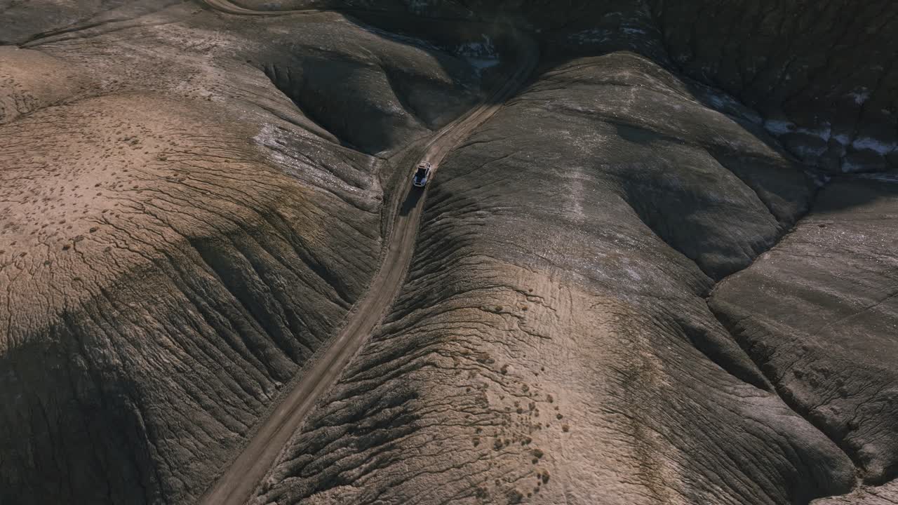 vehículo todoterreno que conduce a lo largo de estrechos desfiladeros entre colinas redondas y arrugadas de paisaje lunar, factory butte en utah, ee.uu.