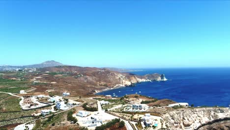 Aerial-4K-Blue-Sea-and-Sky-Top-Flyover-View-of-Village-of-Akra-Mavro-Vouno-with-sailboats-docked-in-Santorini-Greece