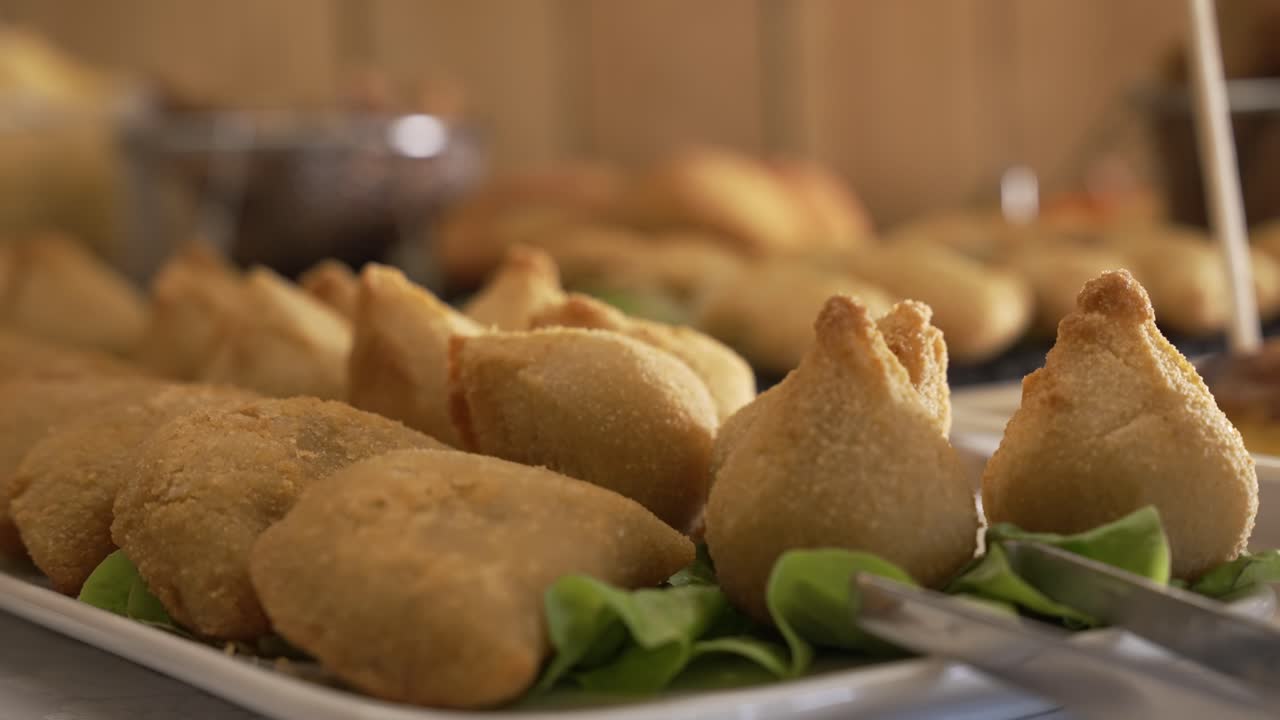 Coxinhas fritte dorate disposte su un vassoio con guarnizione verde per catering.