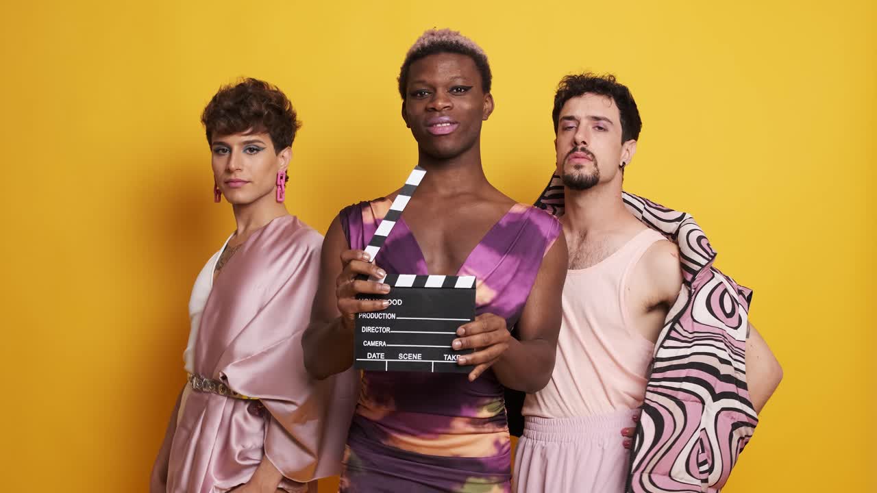 Three transgender male models posing with a film clapperboard
