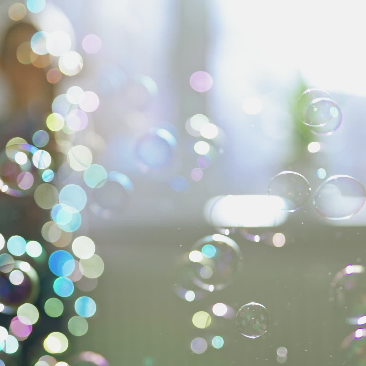 Multi-colored bubbles flying in the room on the blurred background with a boy. A lot of soap bubbles and a child who is playing with them at home. Close-up.