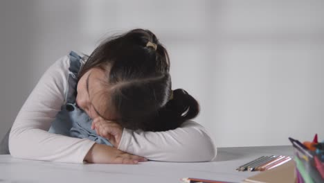 foto de estudio de una chica hiperactiva aburrida sentada en la mesa con fondo blanco 1