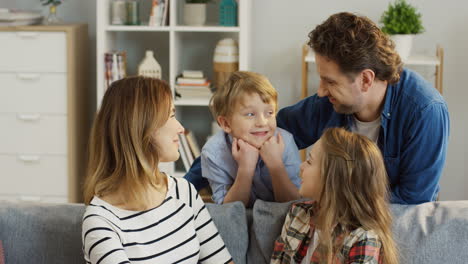 Porträt-Der-Glücklichen-Jungen-Mutter-Und-Des-Vaters,-Die-Mit-Ihrer-Jugendlichen-Hübschen-Tochter-Und-Ihrem-Kleinen-Sohn-Im-Wohnzimmer-Zu-Hause-Sitzen,-Lächeln-Und-Vor-Der-Kamera-Posieren