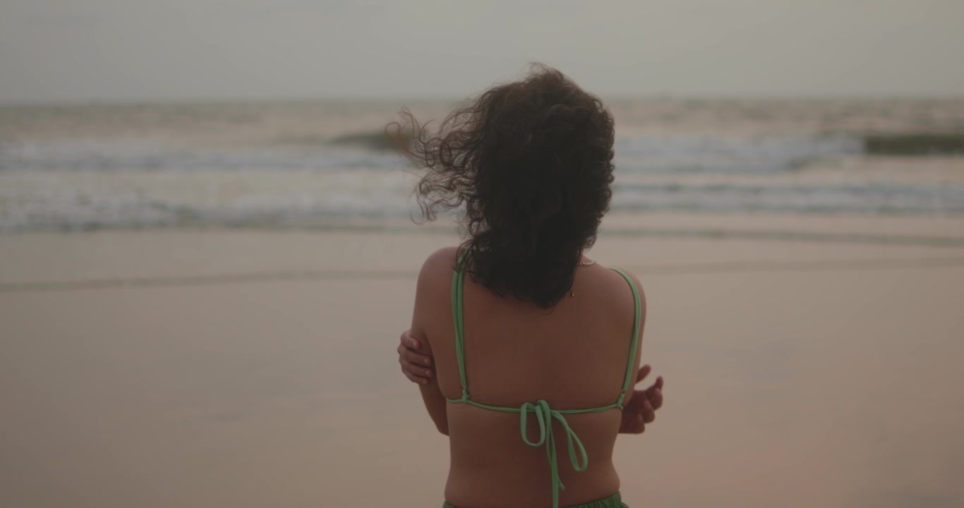 Woman standing on a beach, feeling the ocean breeze and warm sand, gazing at the breaking waves and distant horizon, embracing contemplation and personal space