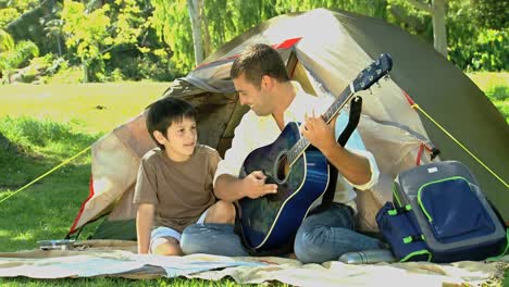 father playing guitar to his son in front of a tent