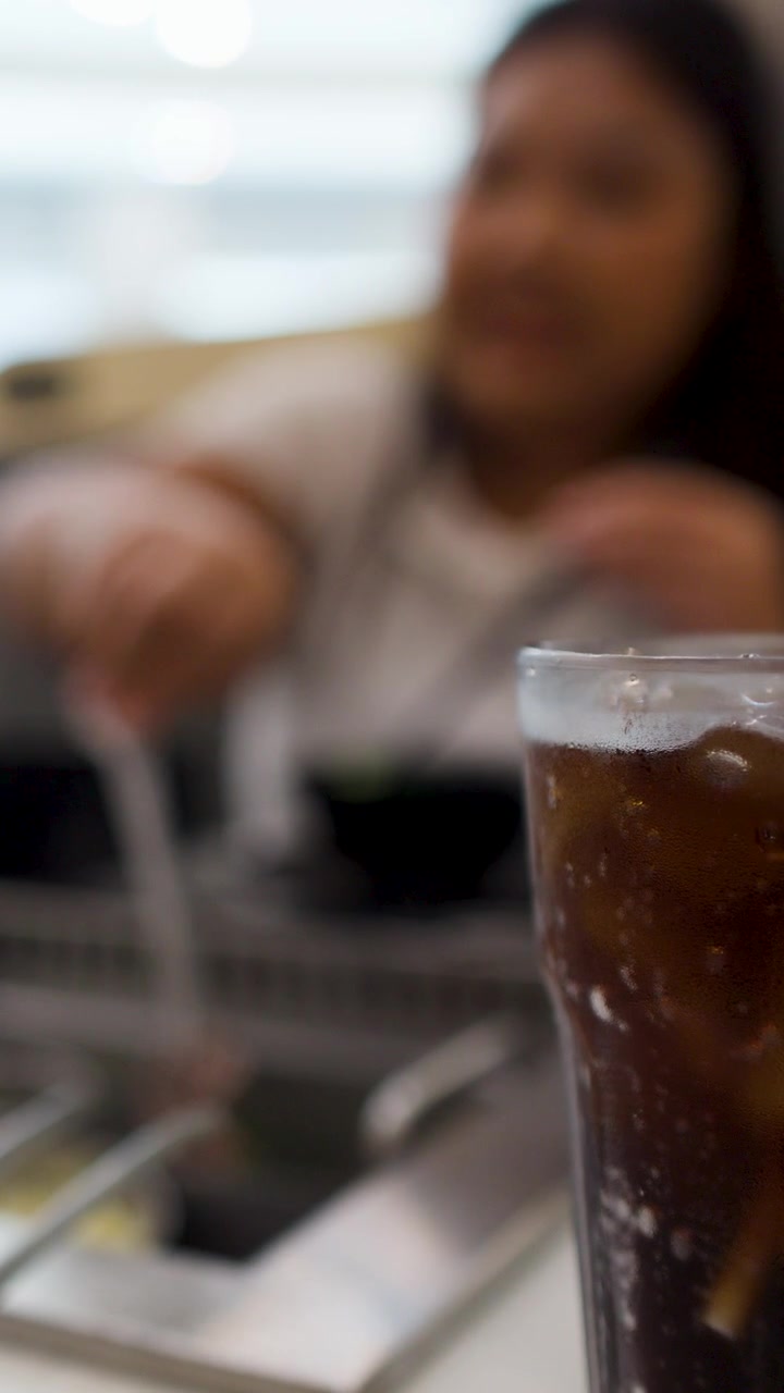 Una cola fredda in primo piano con una donna sfocata che cucina a un tavolo di un ristorante barbecue asiatico.