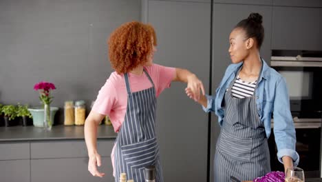 happy diverse couple in aprons having fun cooking and dancing together in kitchen, in slow motion