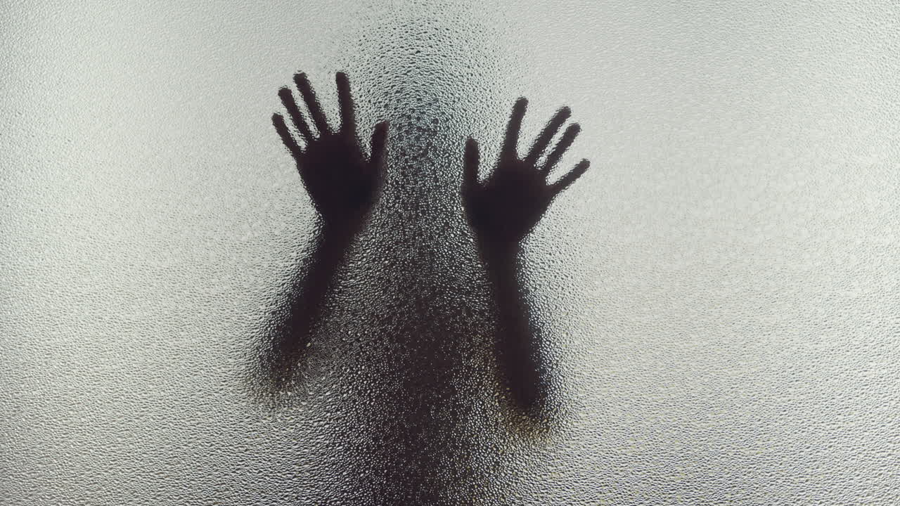 Una silhouette femminile dietro la finestra smerigliata tocca lentamente il vetro.