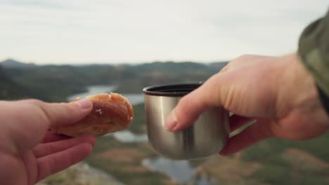 a person holding a stainless steel vacuum flask coffee cup and bread over mountains