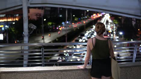 female traveler standing above evening rush hour traffic in bangkok, thailand