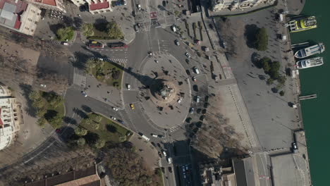 Vista-De-Pájaro-De-Una-Gran-Rotonda-De-Varios-Carriles-Alrededor-De-Un-Famoso-Punto-De-Referencia.-Vehículos-Que-Pasan-Por-El-Monumento-A-Colón.-Barcelona,-España