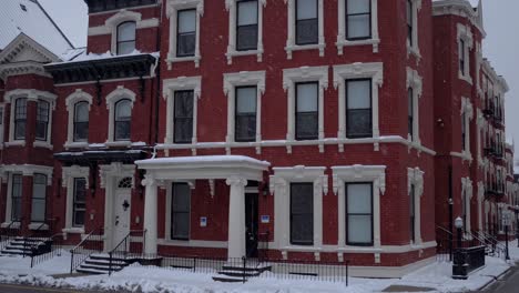 snowflakes drifting over historic red brick residence, highlighting white architectural details, ornate windows, and classic porch during serene winter moment