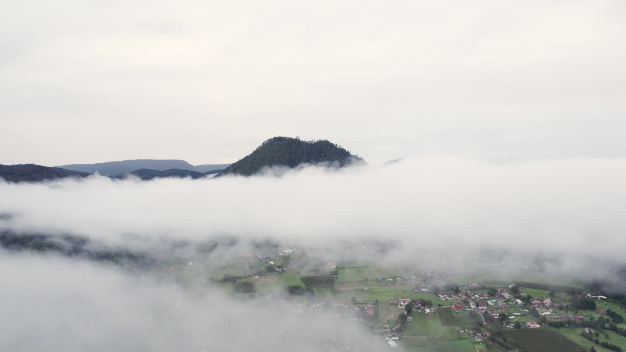 아래 작은 마을과 함께 배경에 산꼭대기와 함께 구름을 통해 공중 드론 총격 비행