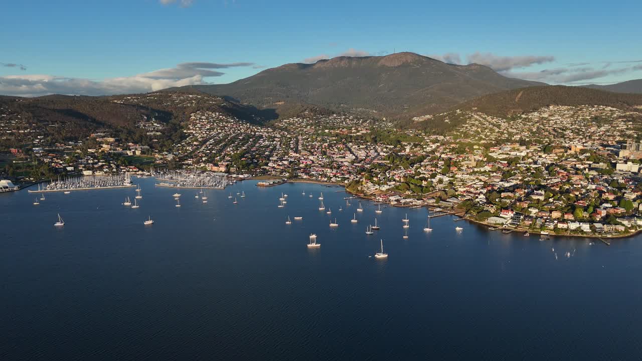 Descending aerial view of Hobart and the Derwent River at sunset. Mountains in the background.