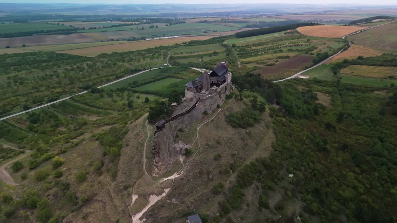 Orbiting aerial view of Boldogkő Castle atop a hill, surrounded by lush greenery, farmland, and a gorgeous rural landscape in Boldogkőváralja, Hungary, showcasing medieval architecture and heritage