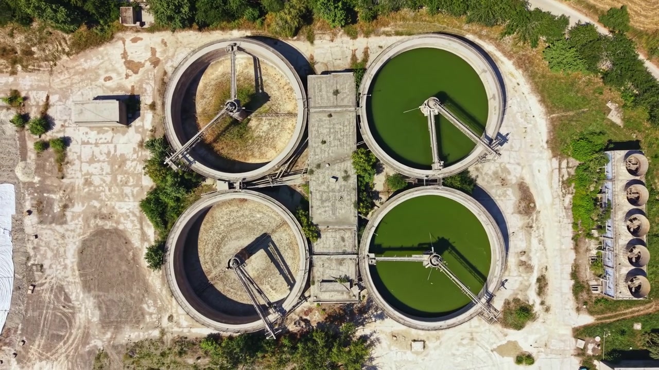 Water treatment facility shows three large circular tanks with different colored water and machinery for processing