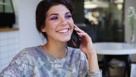 Atractiva-Mujer-Joven-Hablando-Por-Teléfono-Mientras-Está-Sentado-En-La-Cafetería.-Ella-Esta-Sonriendo.-Hermosa-Joven-Teniendo-Una-Conversación-Informal