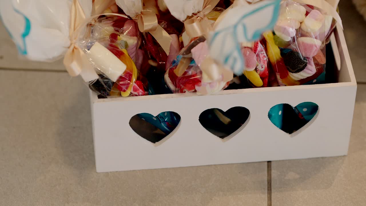 close up of assorted candy bags in white box with heart cutouts on tiled floor