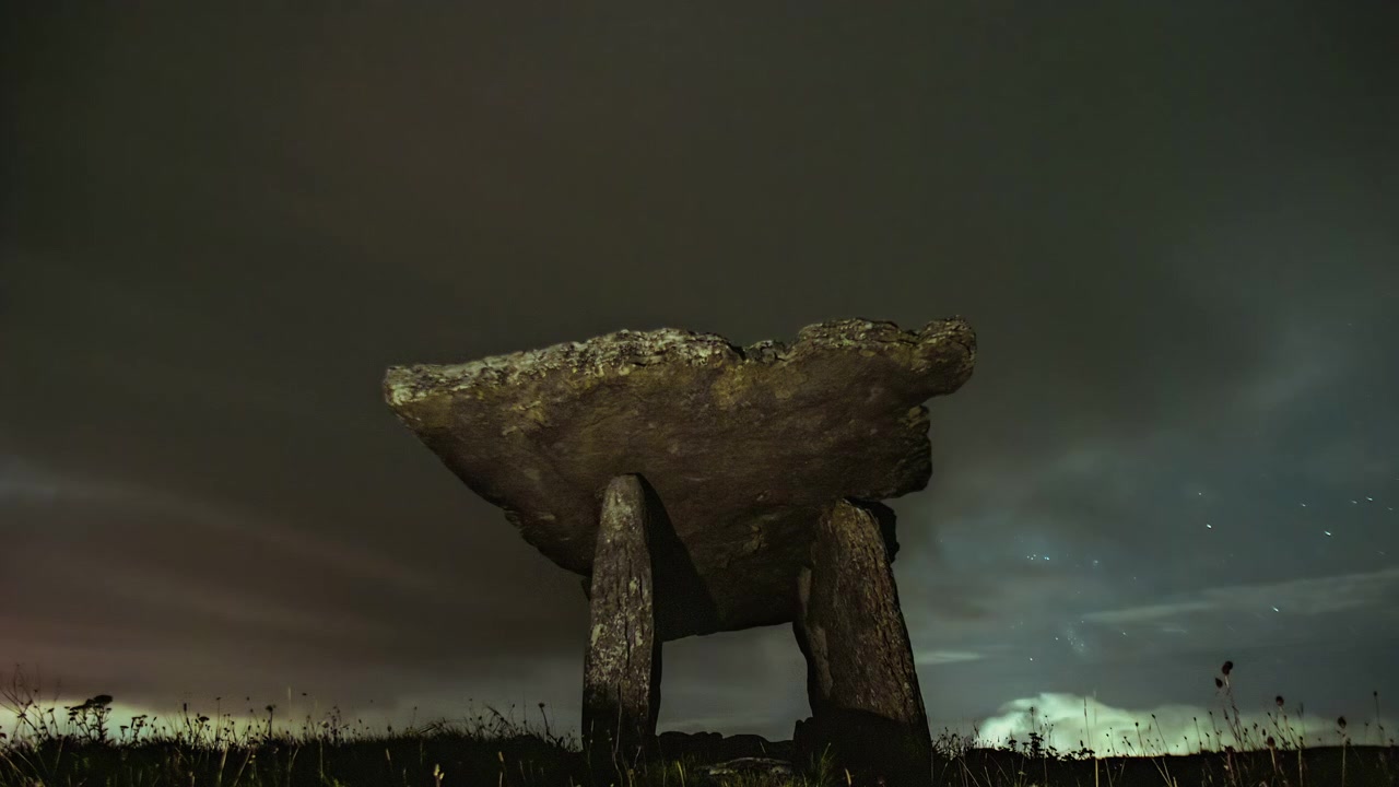 Nocny timelapse dolmenu Poulnabrone w Burren, gdy chmury unoszą się po gwieździstym niebie, ukazując nastrojową atmosferę wiejskiej Irlandii.