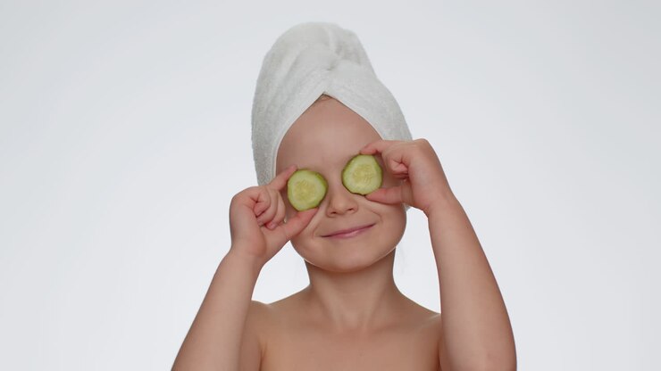 Smiling child girl kid holding slices of cucumber, covering eyes, natural cosmetics, face skin care