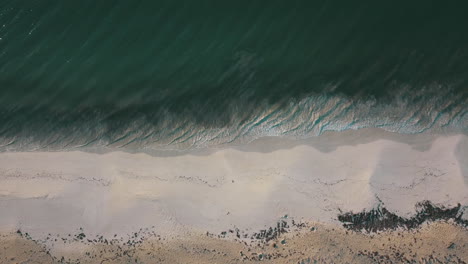 midday static drone shot of waves crashing onto the beach.