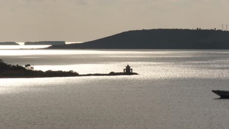 a ferry boat passing in front of an old venetian lighthouse at sunset in argostoli, kefalonia