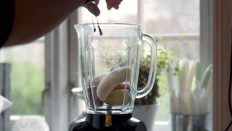 persona poniendo ingredientes saludables en una licuadora para mezclar un batido saludable