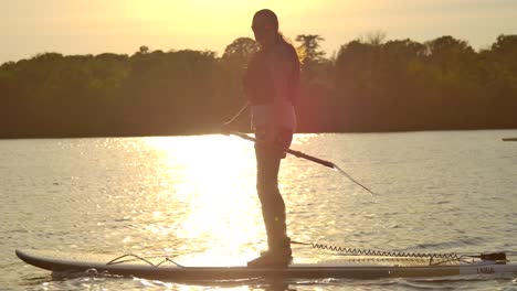 mujer standup paddle boarding en vista lateral del atardecer siguiendo slomo