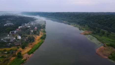 drone shot of a wide nemunas river with a green forest and houses on the bank on a cloudy day