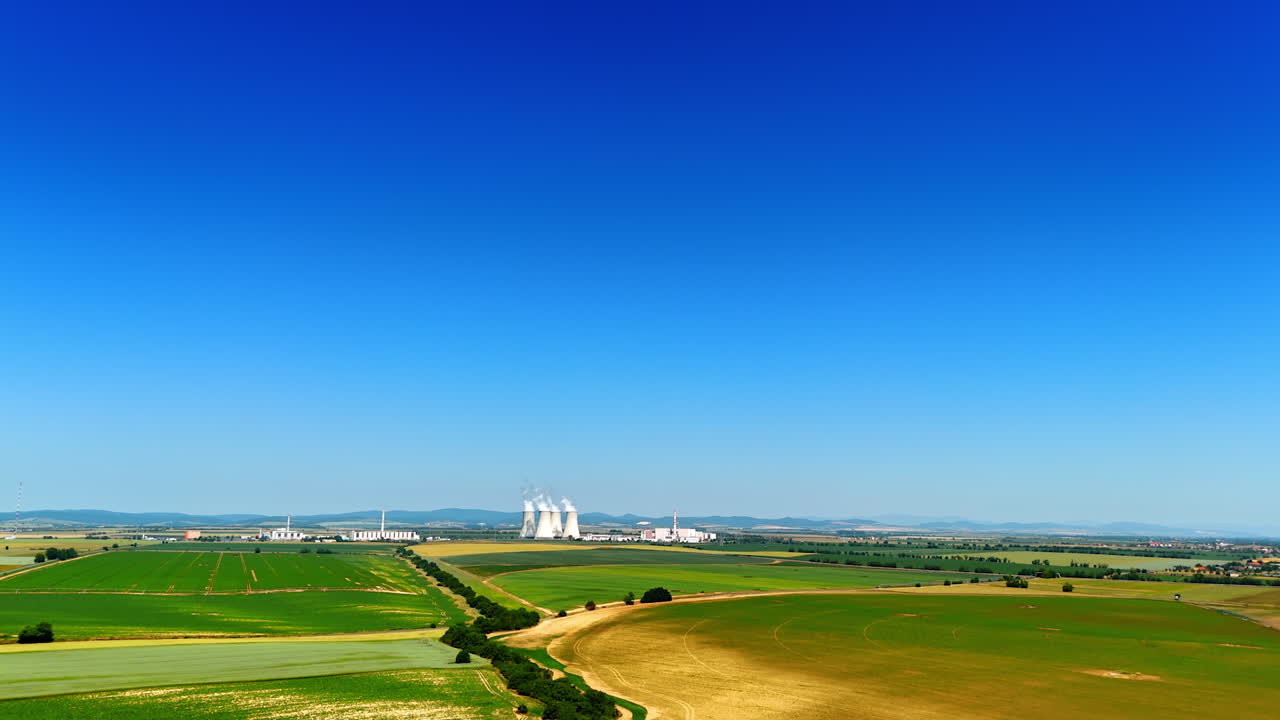 Rising over the vast green field on sunny clear day. Revealing view on the factory pipes producing white smoke