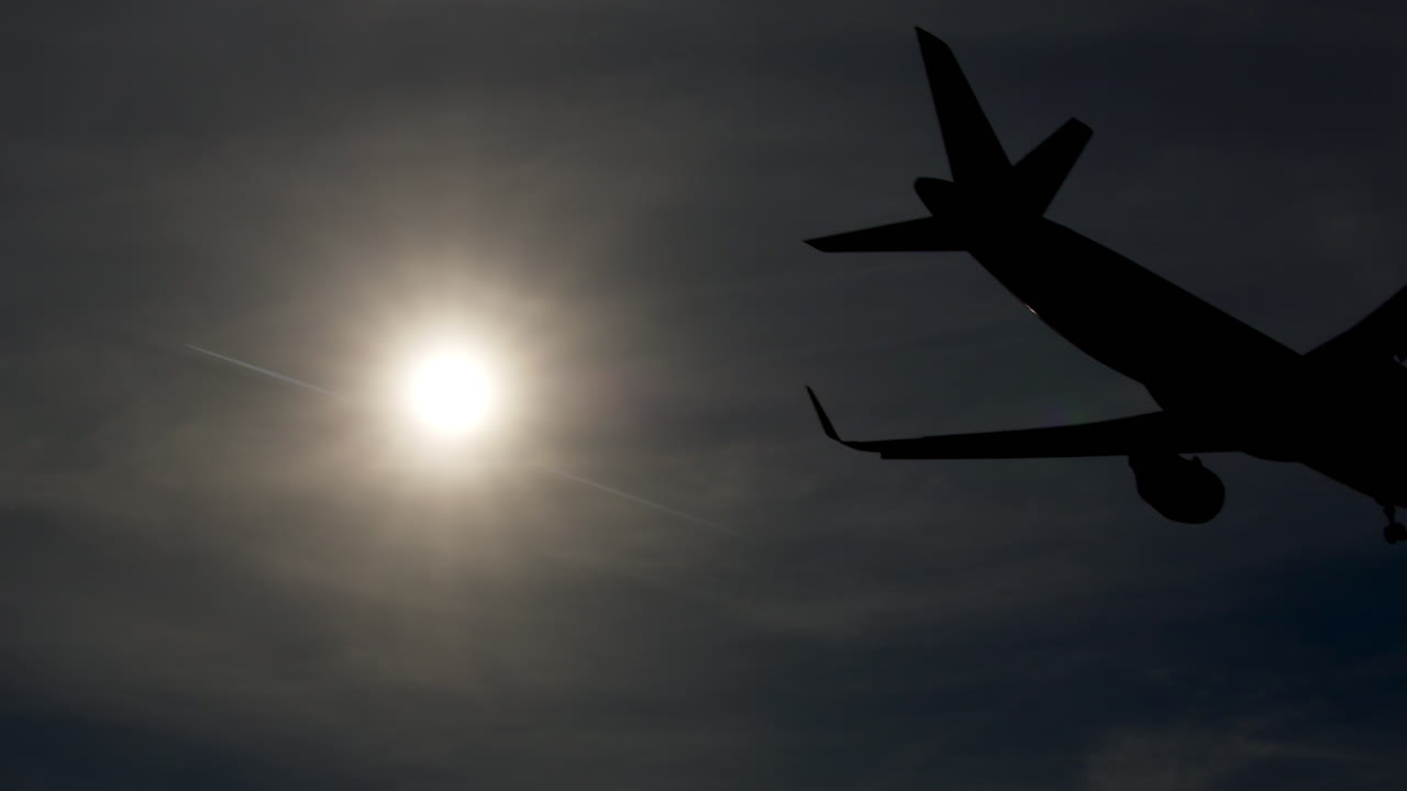 Airplane Silhouette Against Cloudy Sky with Sun