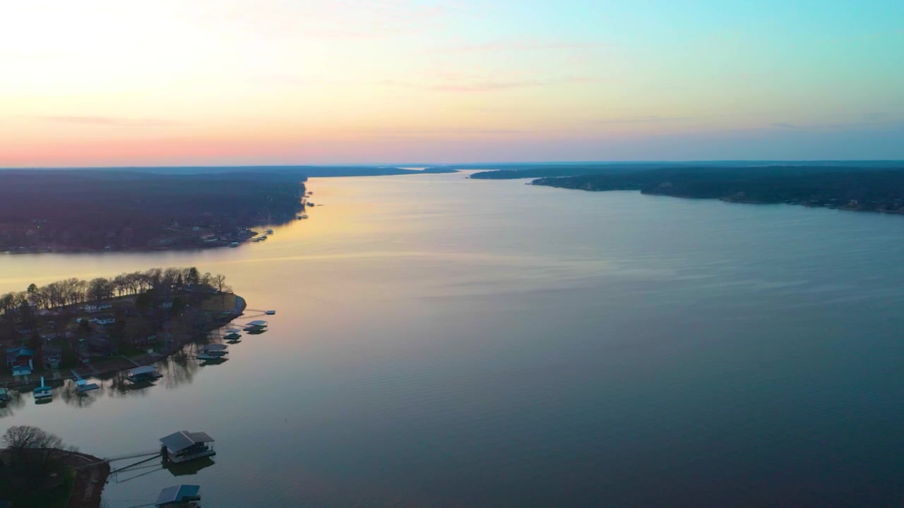 Vista aerea da drone sopra il Lago Cumberland al tramonto, che mostra l'acqua calma, la costa boscosa del Kentucky, le case galleggianti ormeggiate, le case sul lago e i tenui colori del tramonto sul bacino idrico.